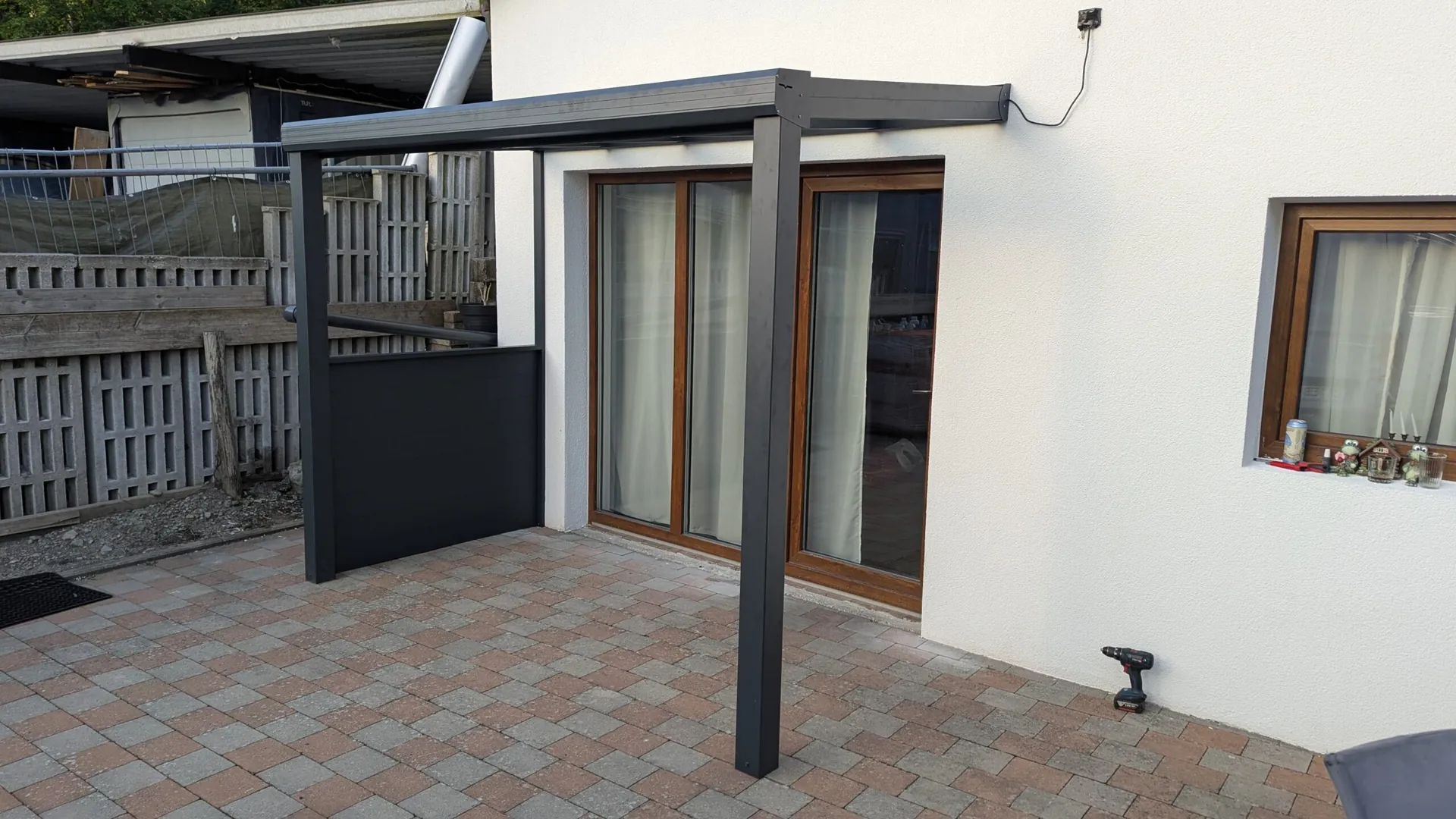 Dunkle Terrassenüberdachung mit seitlichem Sichtschutz vor einer breiten Terrassentür.