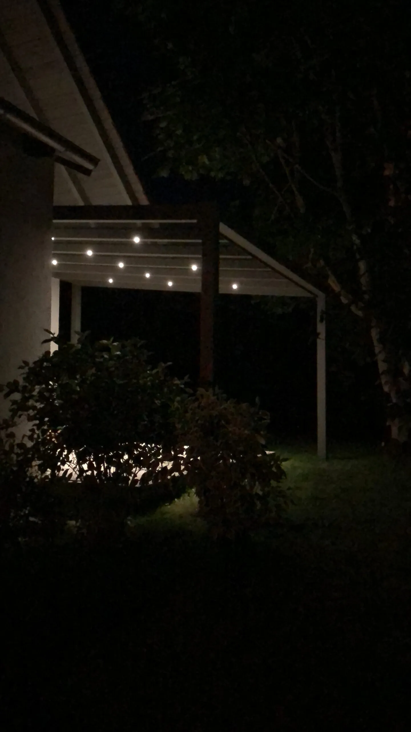 Terrassenüberdachung bei Nacht: Integrierte Leuchten erhellen den Sitzbereich neben dem Garten.
