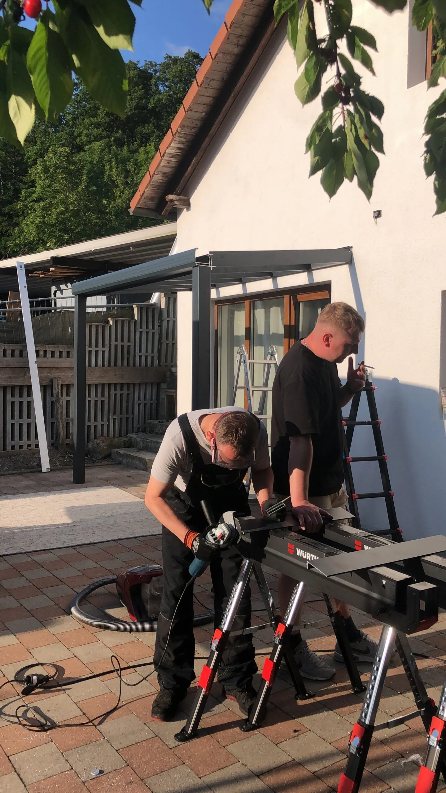 Zwei Personen bearbeiten ein Metallprofil vor einer Terrassenüberdachung.